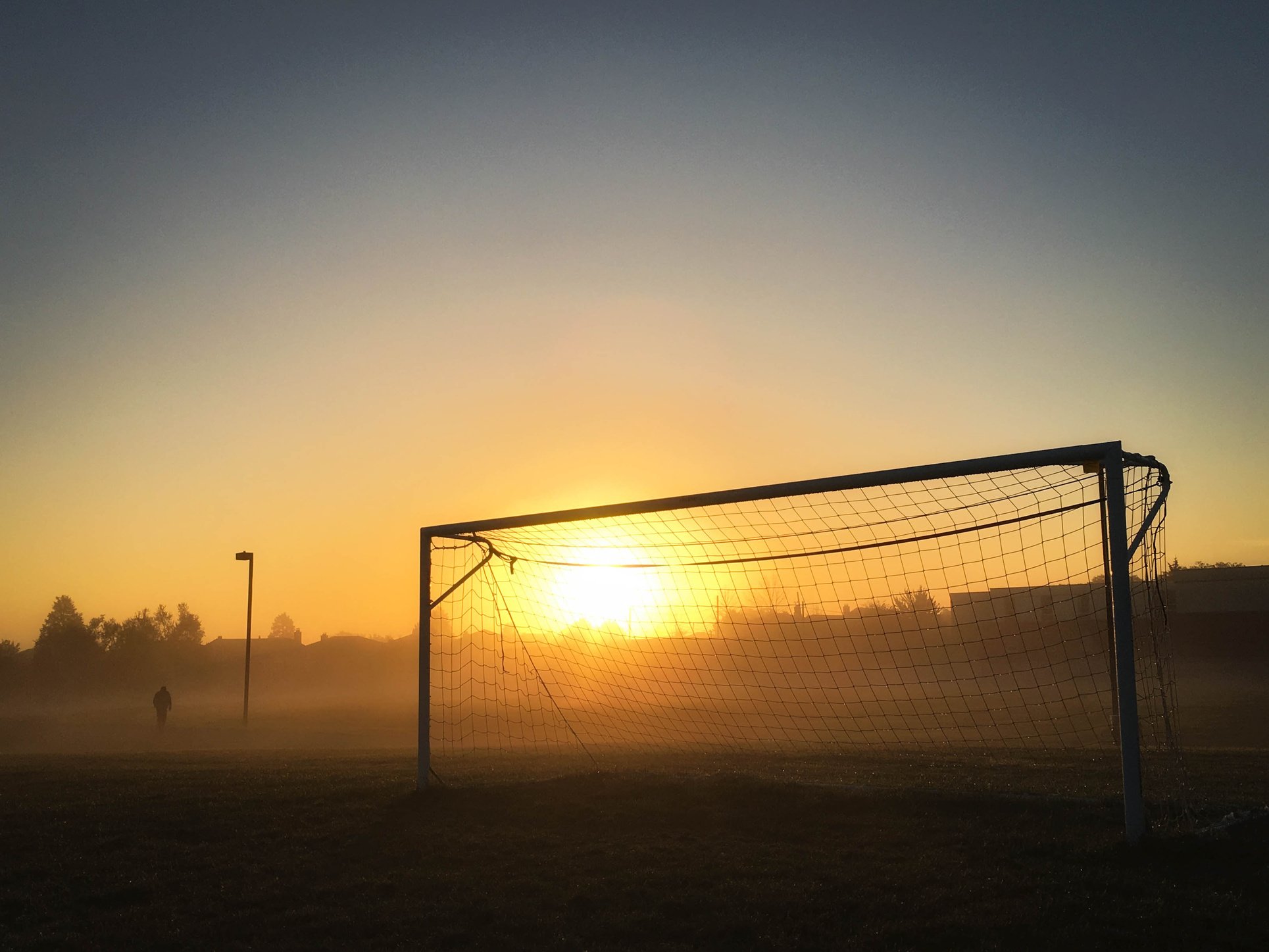 Person Jogging Near Soccer Goal during Sunrise